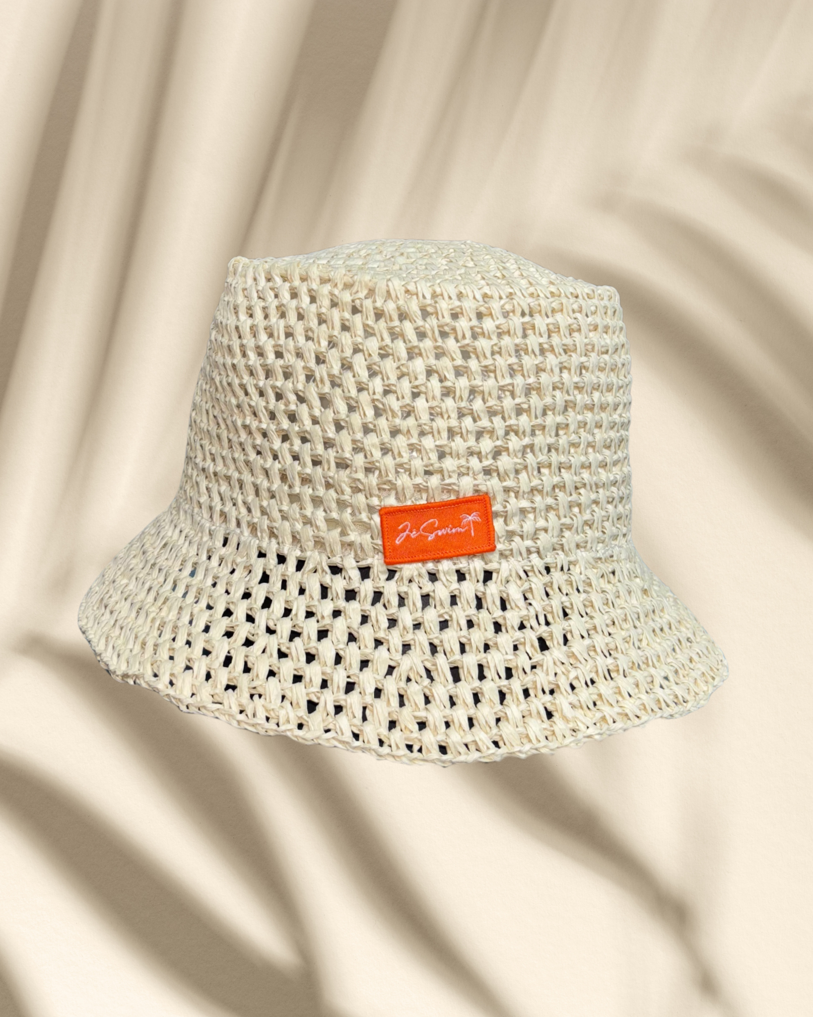 Natural bucket hat with a brand label on a peach-colored background