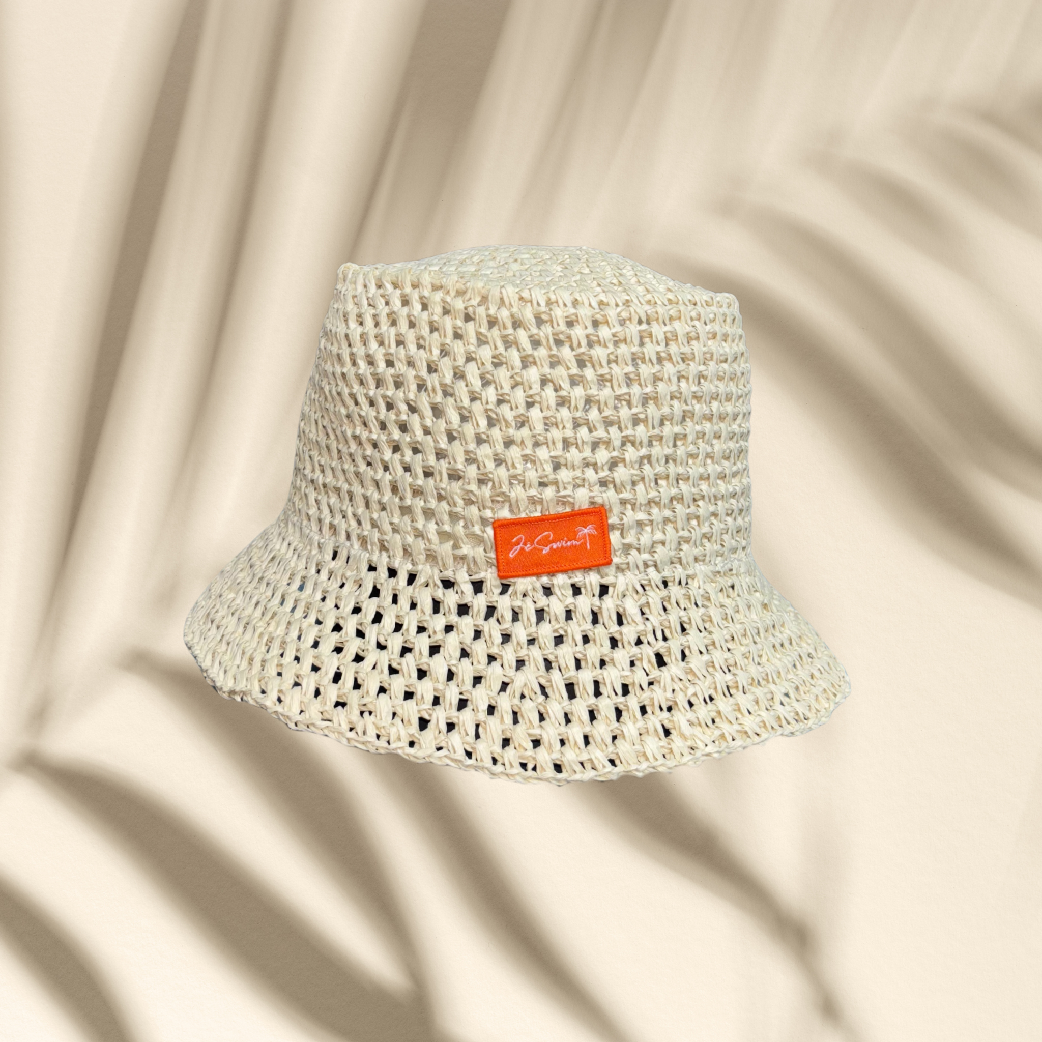 Natural bucket hat with a brand label on a peach-colored background