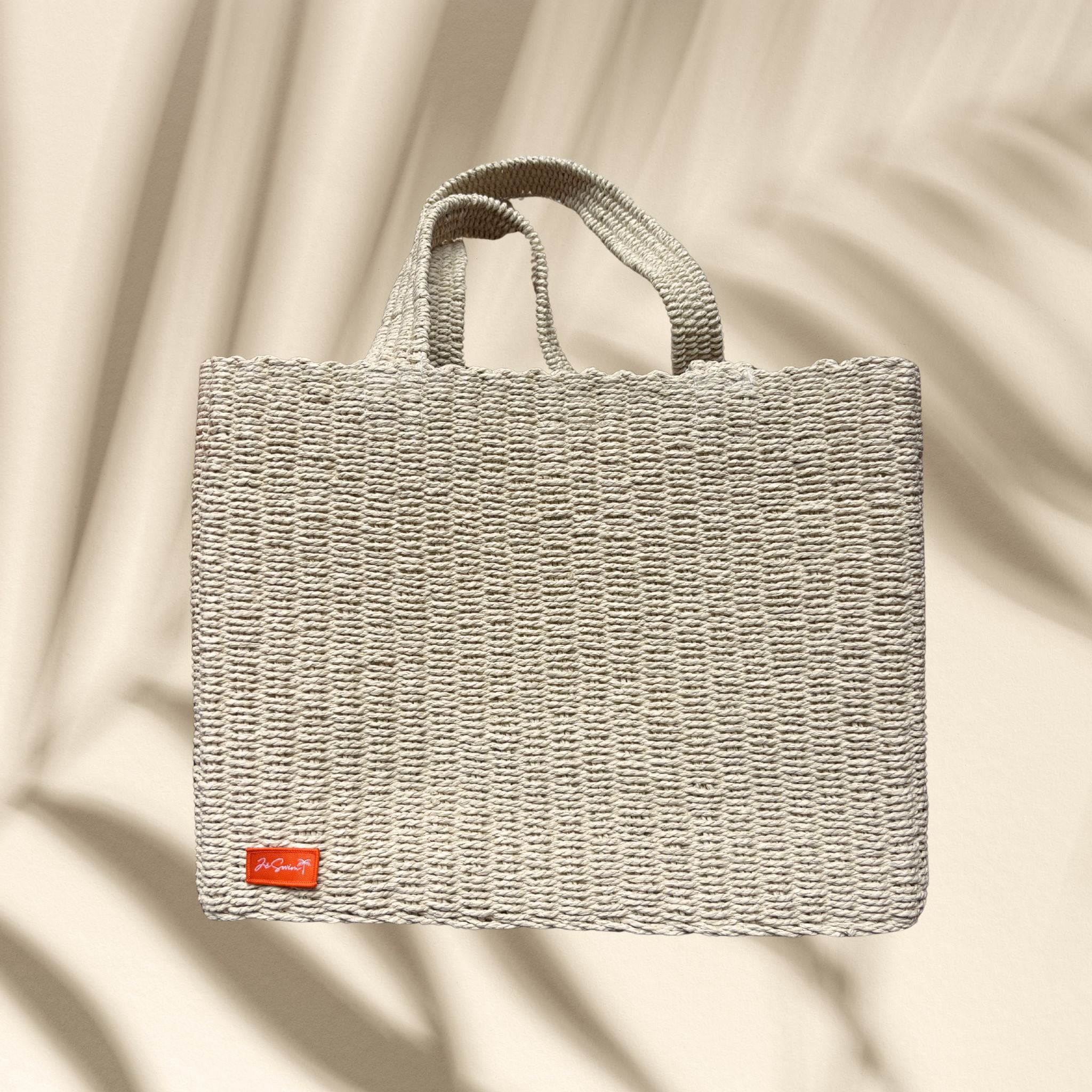 Natural Raffia Woven beach bag with a visible brand logo on an orange background