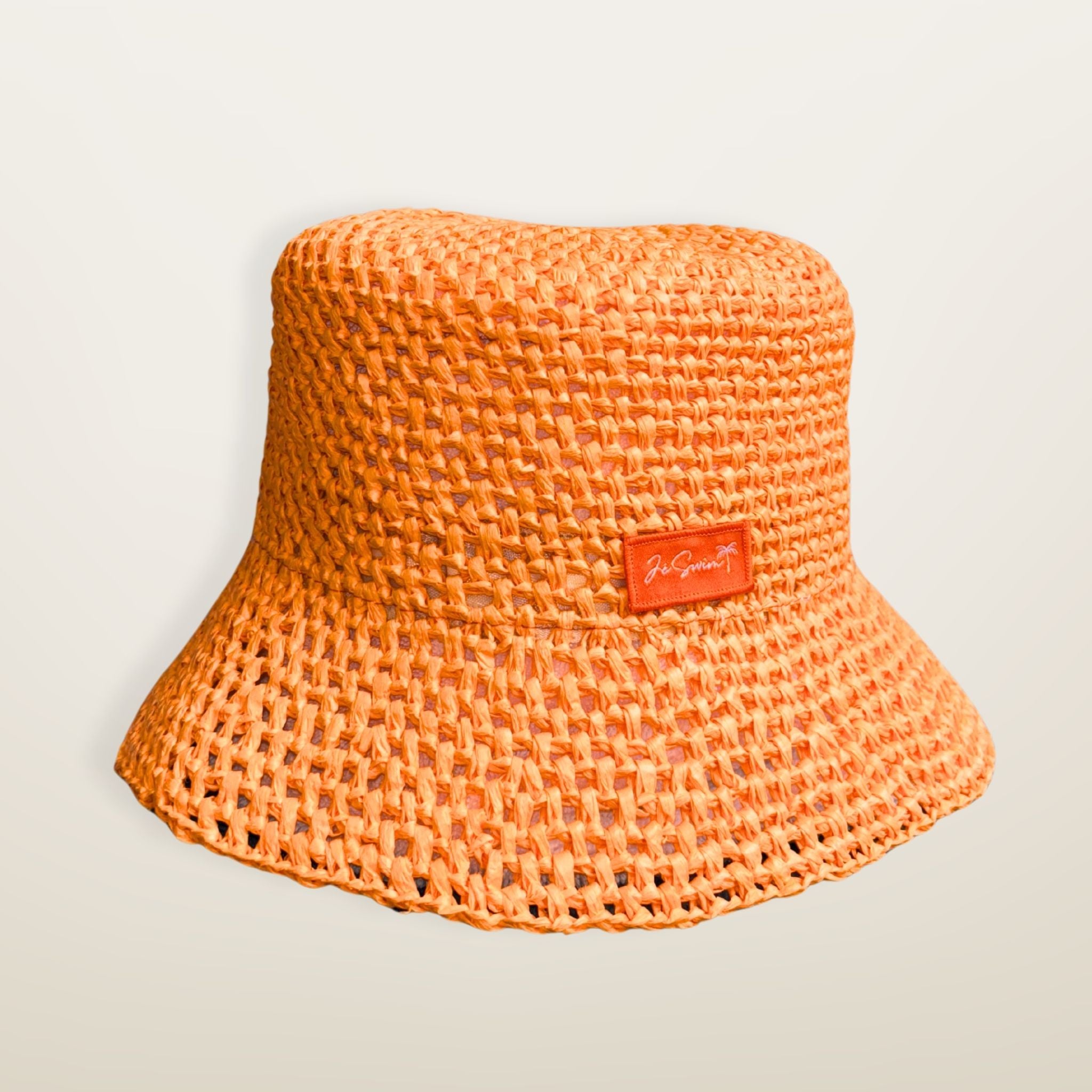 Orange woven RAFFIA bucket hat with a JE brand label on a light beige background