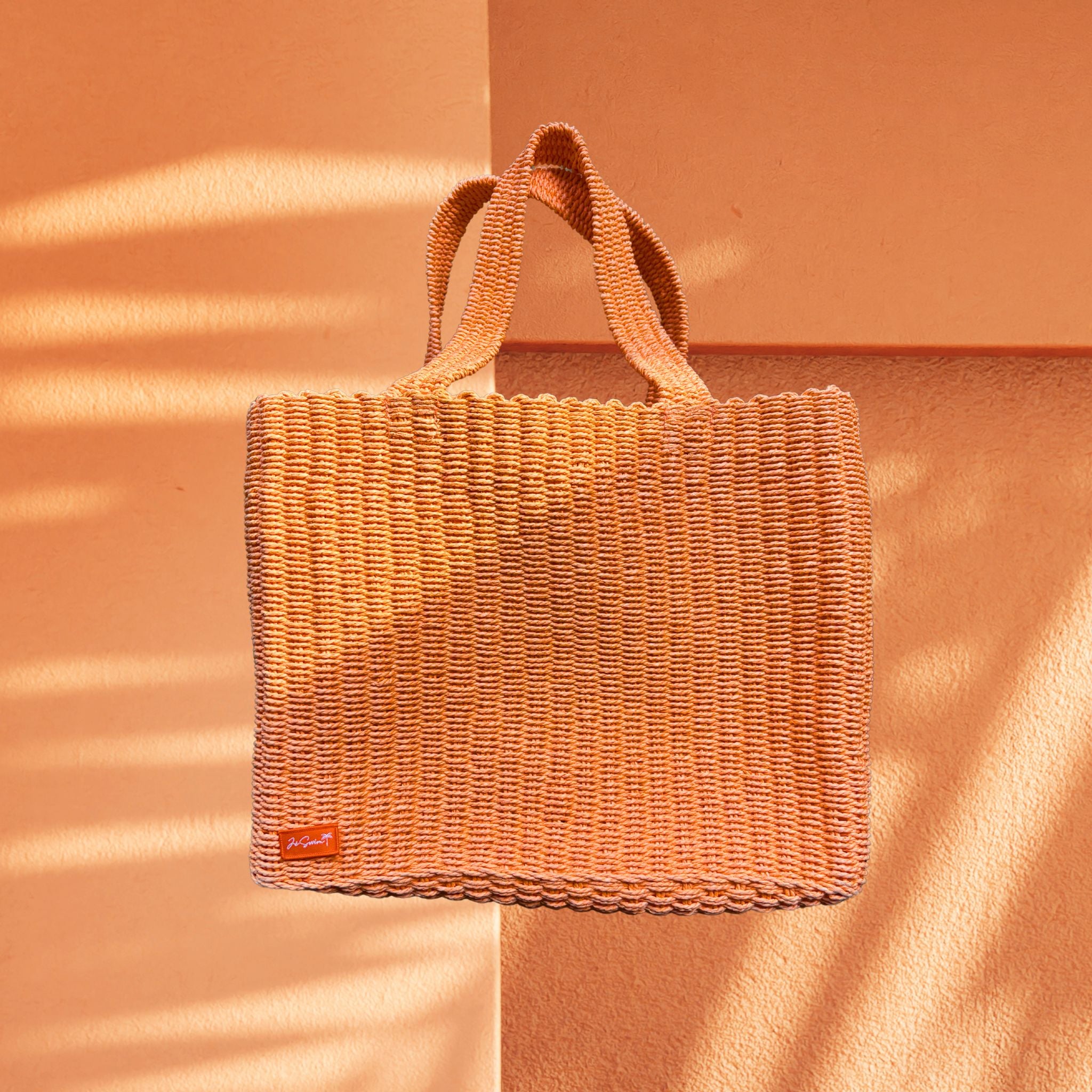 Orange Raffia Woven handbag with a visible brand logo on an orange background
