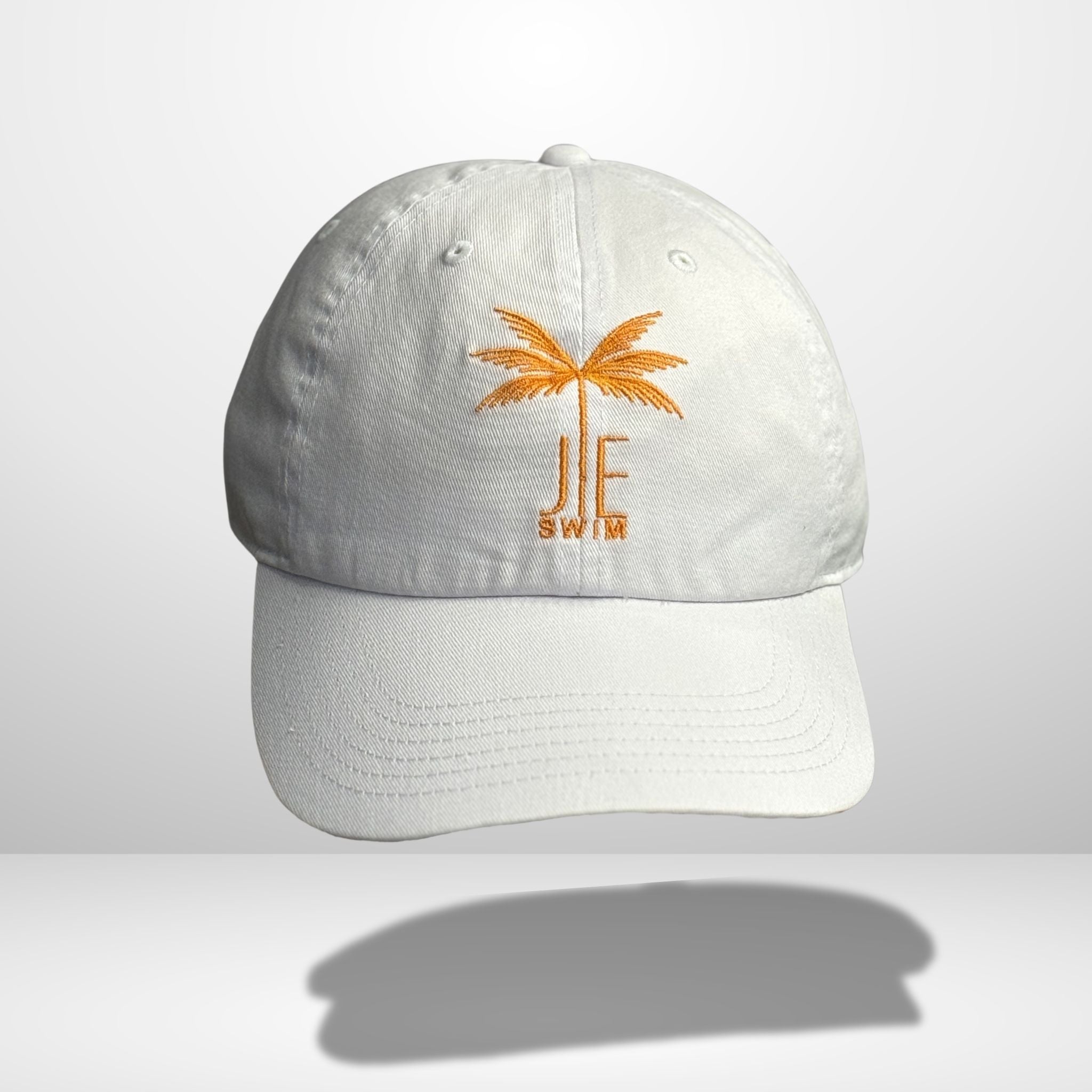 White cotton baseball cap with orange embroidered palm tree and 'JE SWIM' logo on front, featuring curved brim and classic six-panel construction, photographed against clean white background.