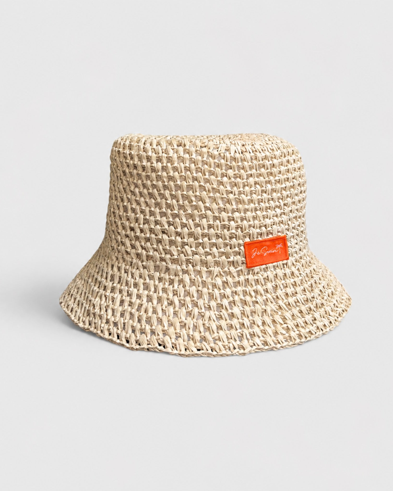 Natural Brown woven bucket hat with an orange label on a light gray background