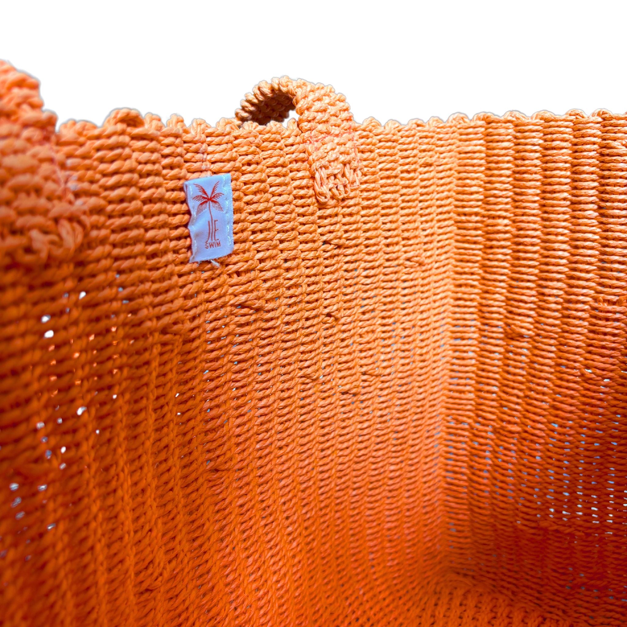 Close-up of an orange raffia bag with a brand label on a white background