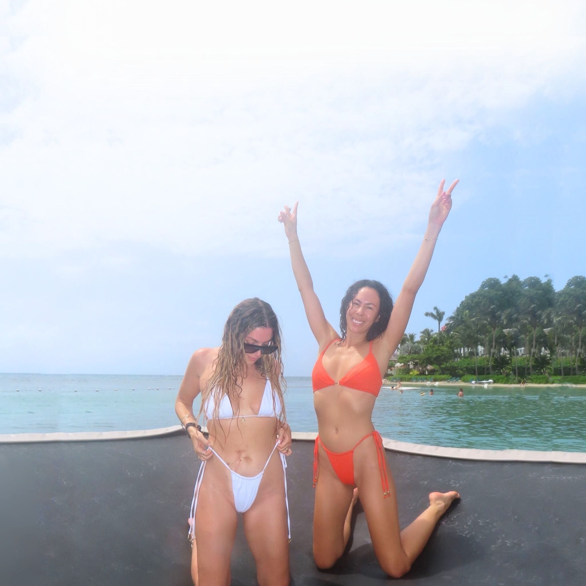 Two women in Je Swim bikinis on a water trampoline at a resort in Jamaica, scenic background